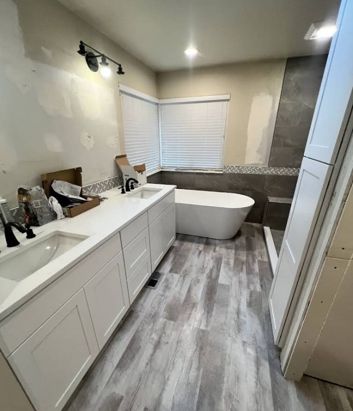 Bathroom renovation with white vanity, gray flooring, bathtub, and partially tiled walls.