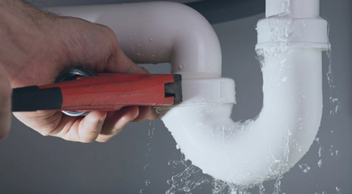 Man in blue overalls operating machinery, wearing black gloves. Inside a workshop.