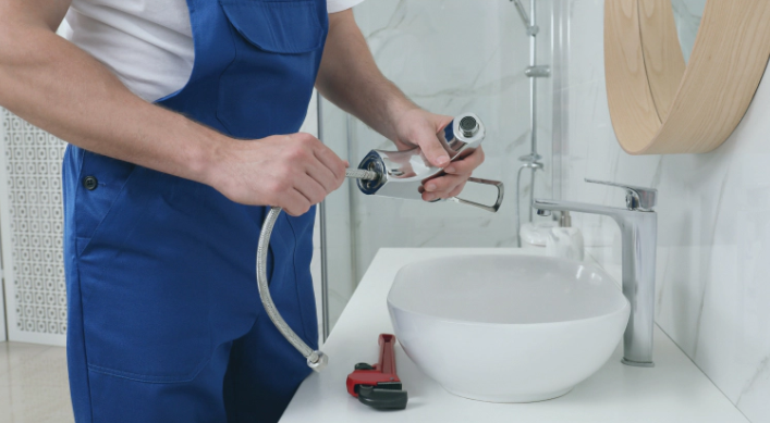 Kitchen sink with open cabinet showing plumbing, blue cabinets, silver faucet, and light countertop.
