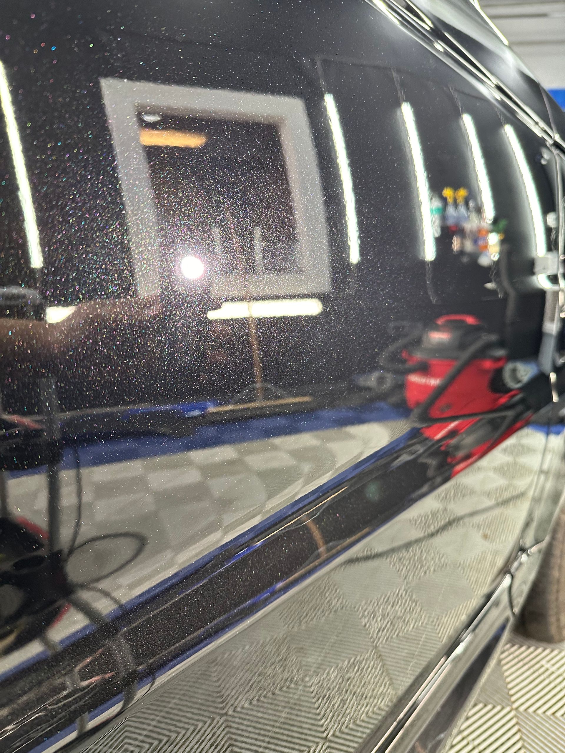 Black car side mirror and glossy door reflecting a garage, with a red bag on the seat inside.