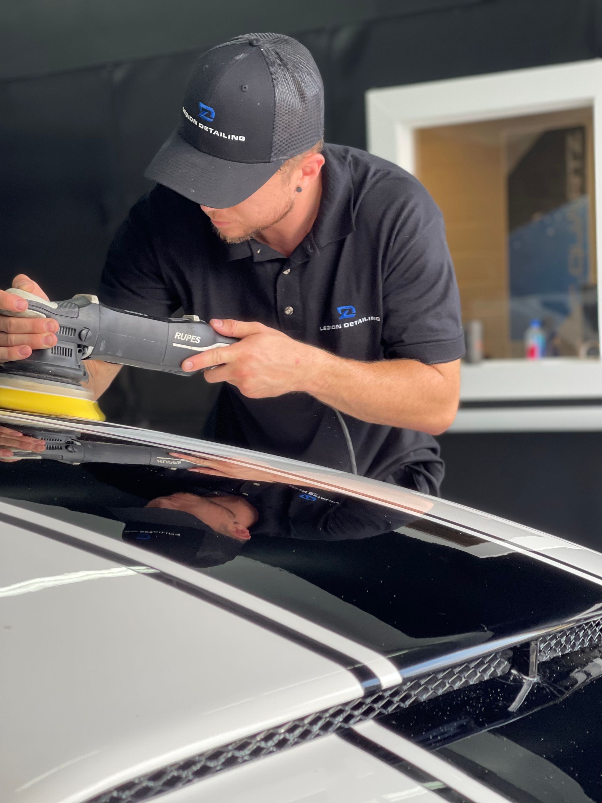 Mechanic polishing a black car roof with a buffer in a garage