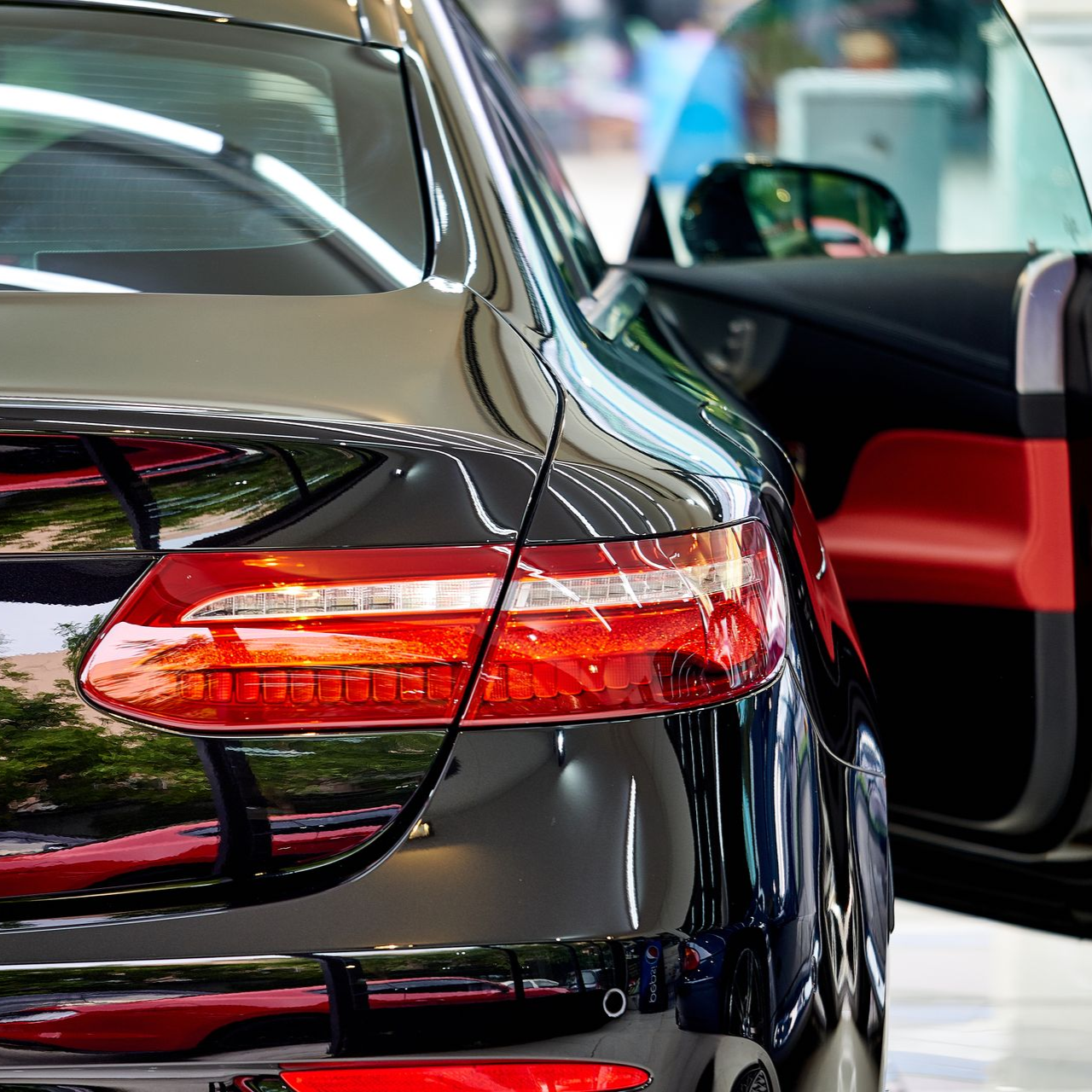 Rear view of a black car with red taillights, parked in a showroom with the door open.