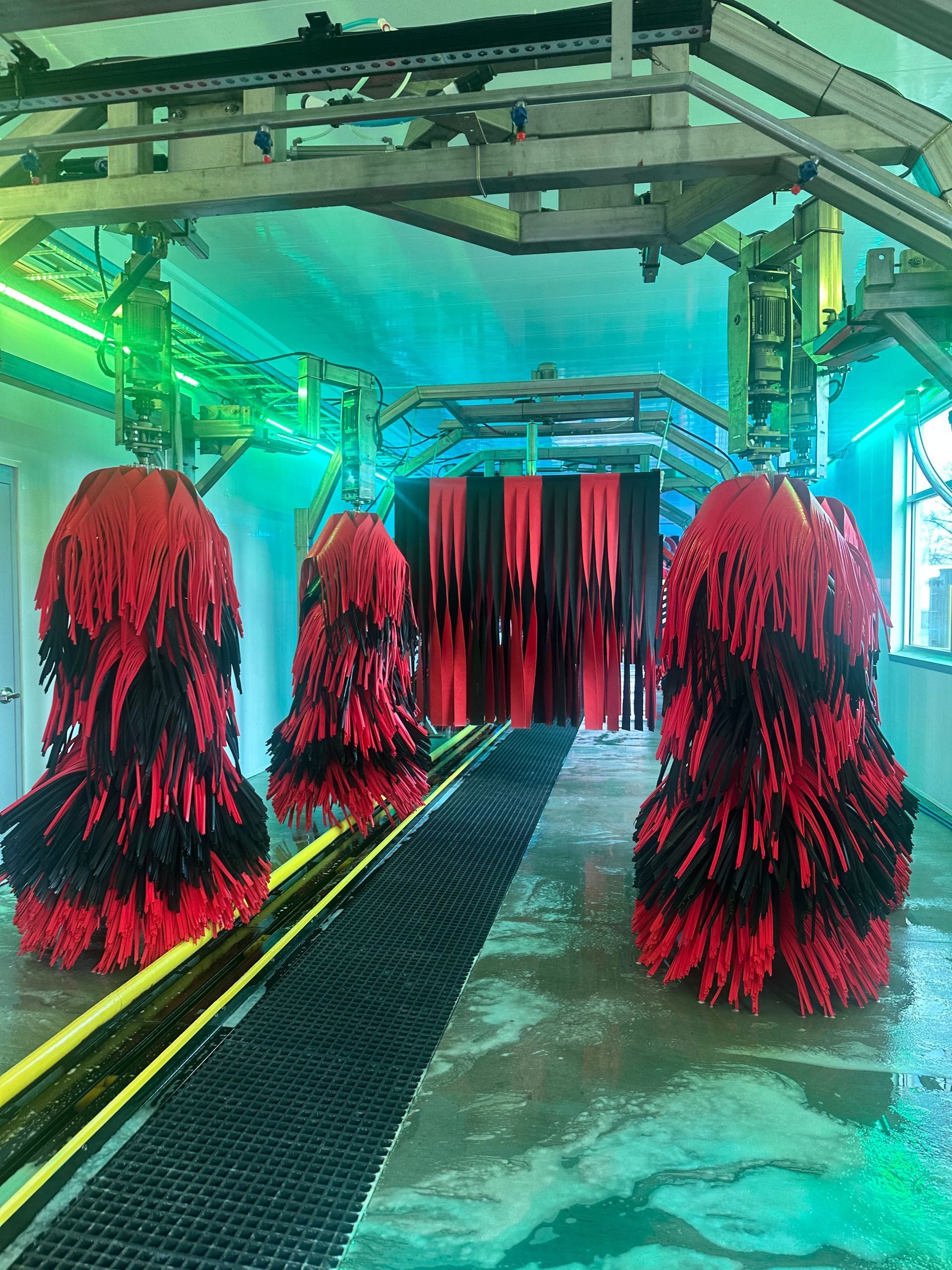 A car wash with red and black brushes hanging from the ceiling.