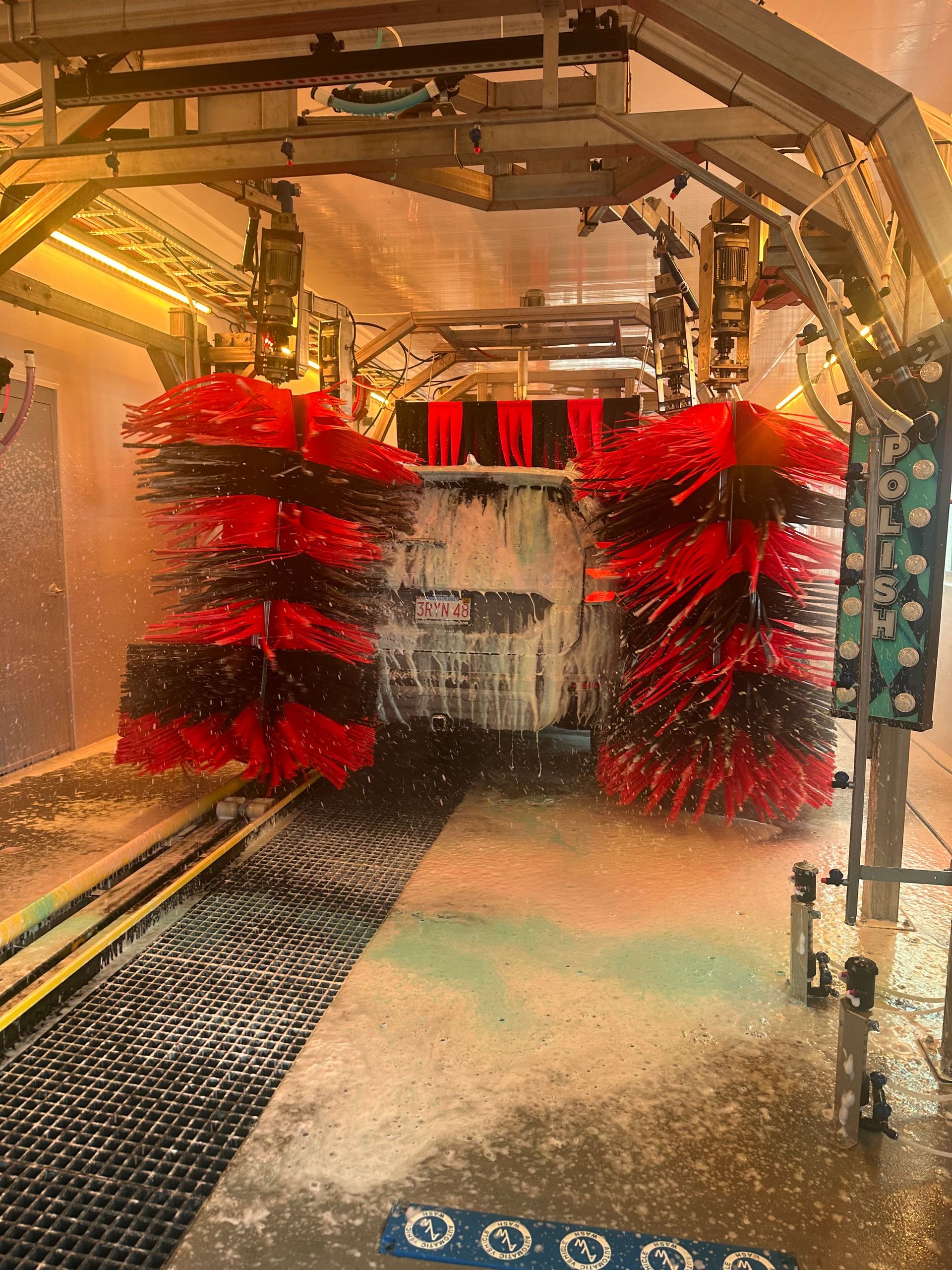 A car is going through a car wash with red brushes