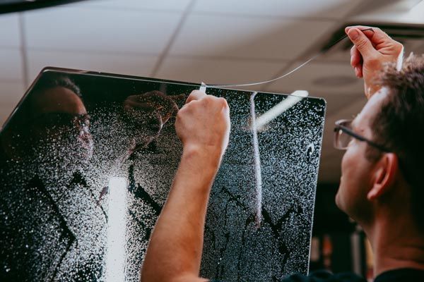 Person cleaning a cracked glass panel with a cloth, seen in close-up indoors