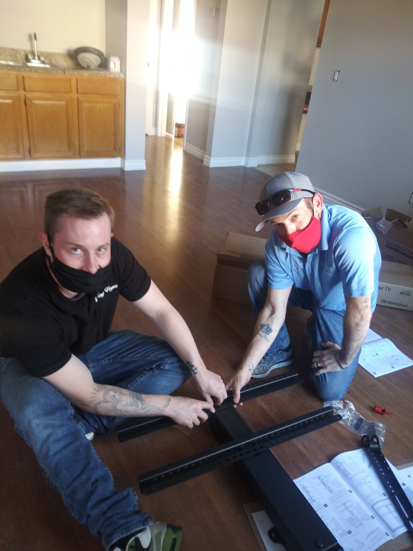 two men wearing face masks are working on a tv mount