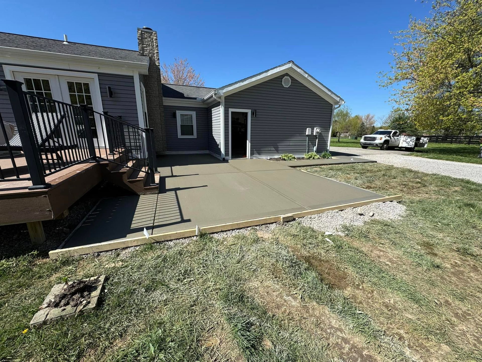 Backyard patio beside a house and detached garage, with concrete slab and grassy yard.