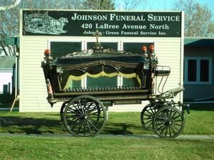 Hearse in front of Johnson Funeral Service sign, on green grass.