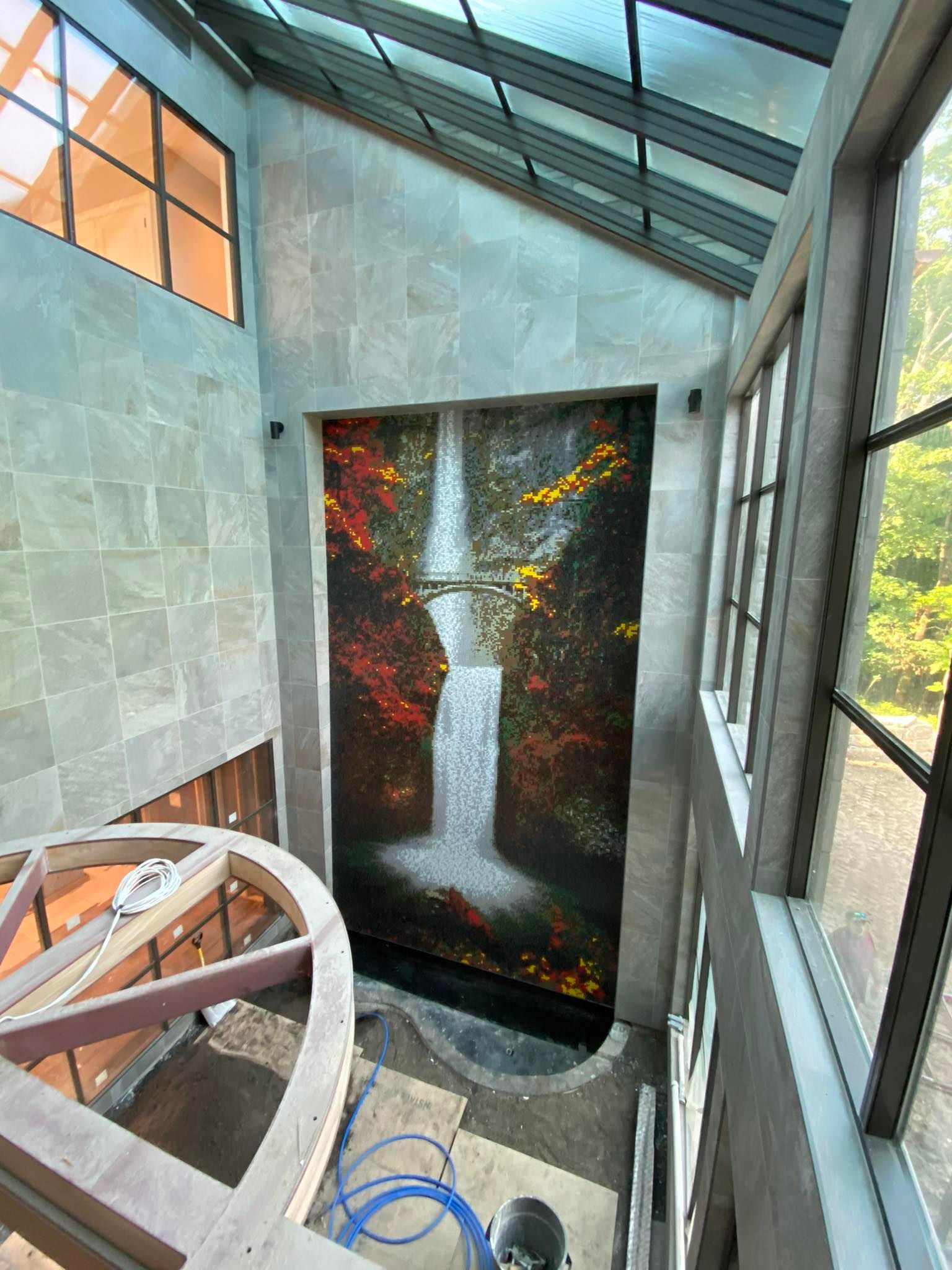 Waterfall mural inside a building with glass ceiling and windows, wooden beams, and grey stone walls.