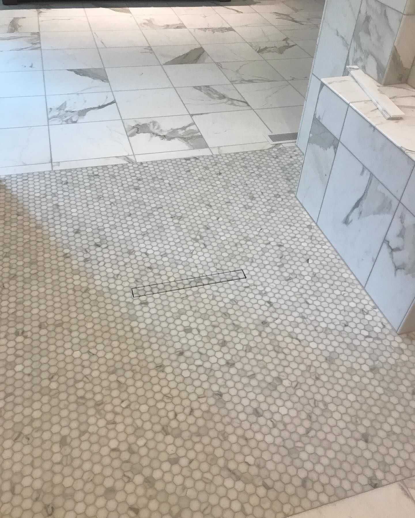 Bathroom floor with white marble tiles and a shower entrance with small, round mosaic tiles.