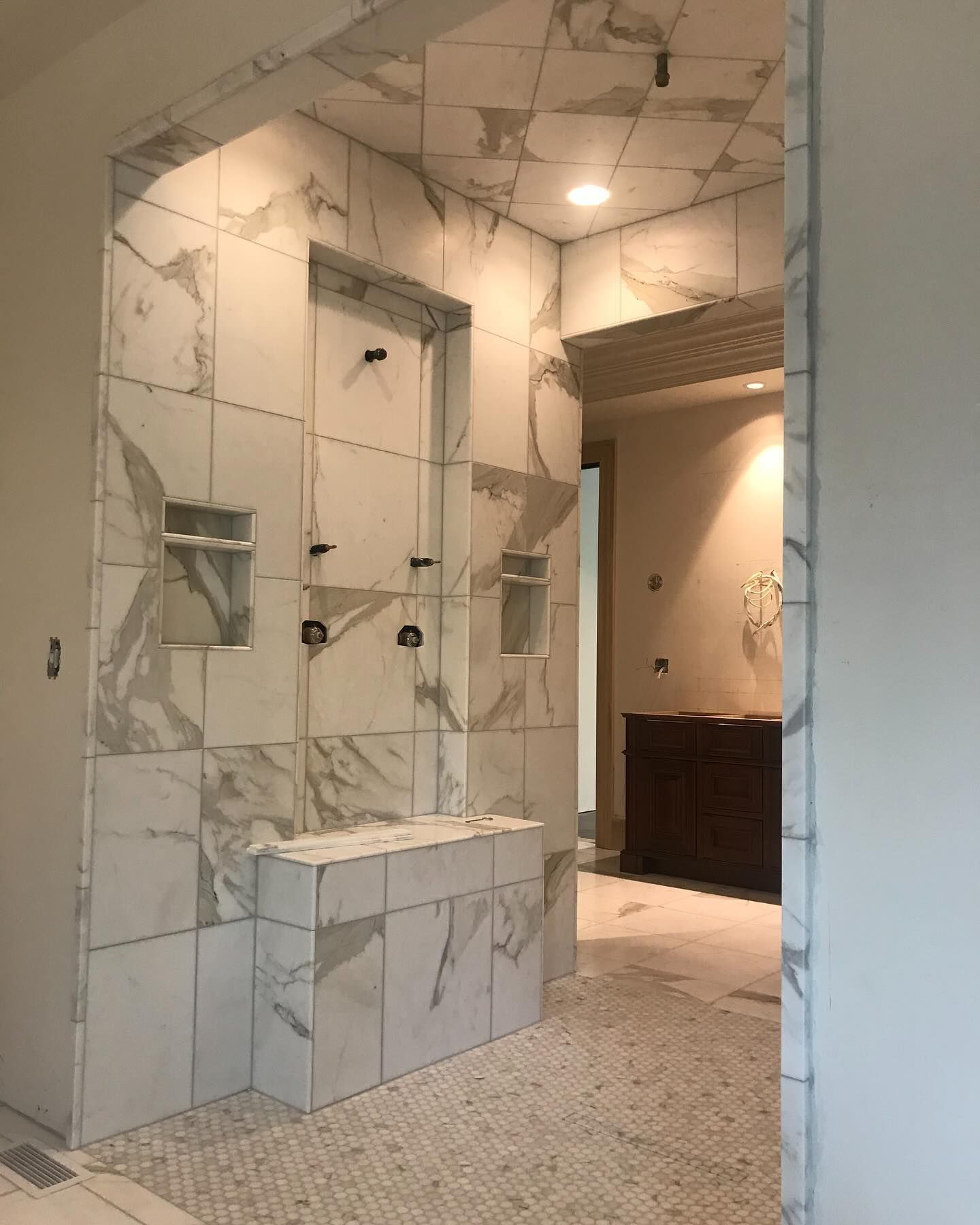 Bathroom under construction with white marble tile, shower fixtures, and doorway.