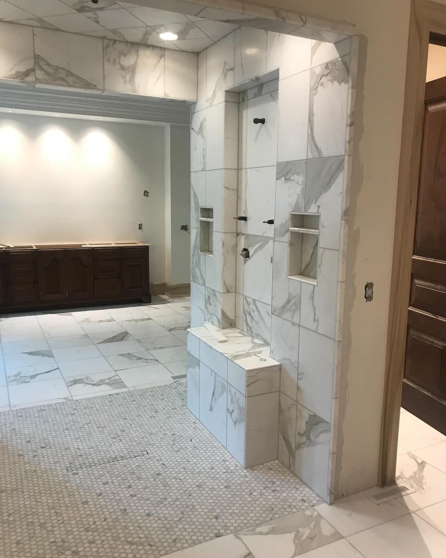 Bathroom with marble-look tile; shower with built-in bench and niches, and a dark wood vanity.
