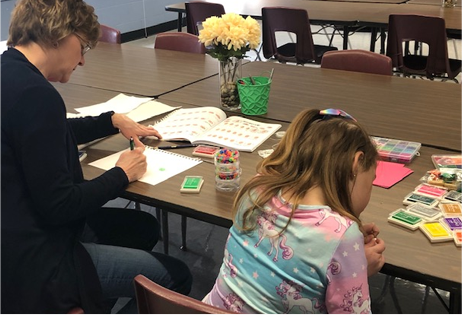 Two people seated at a table sorting colorful cards in a classroom setting