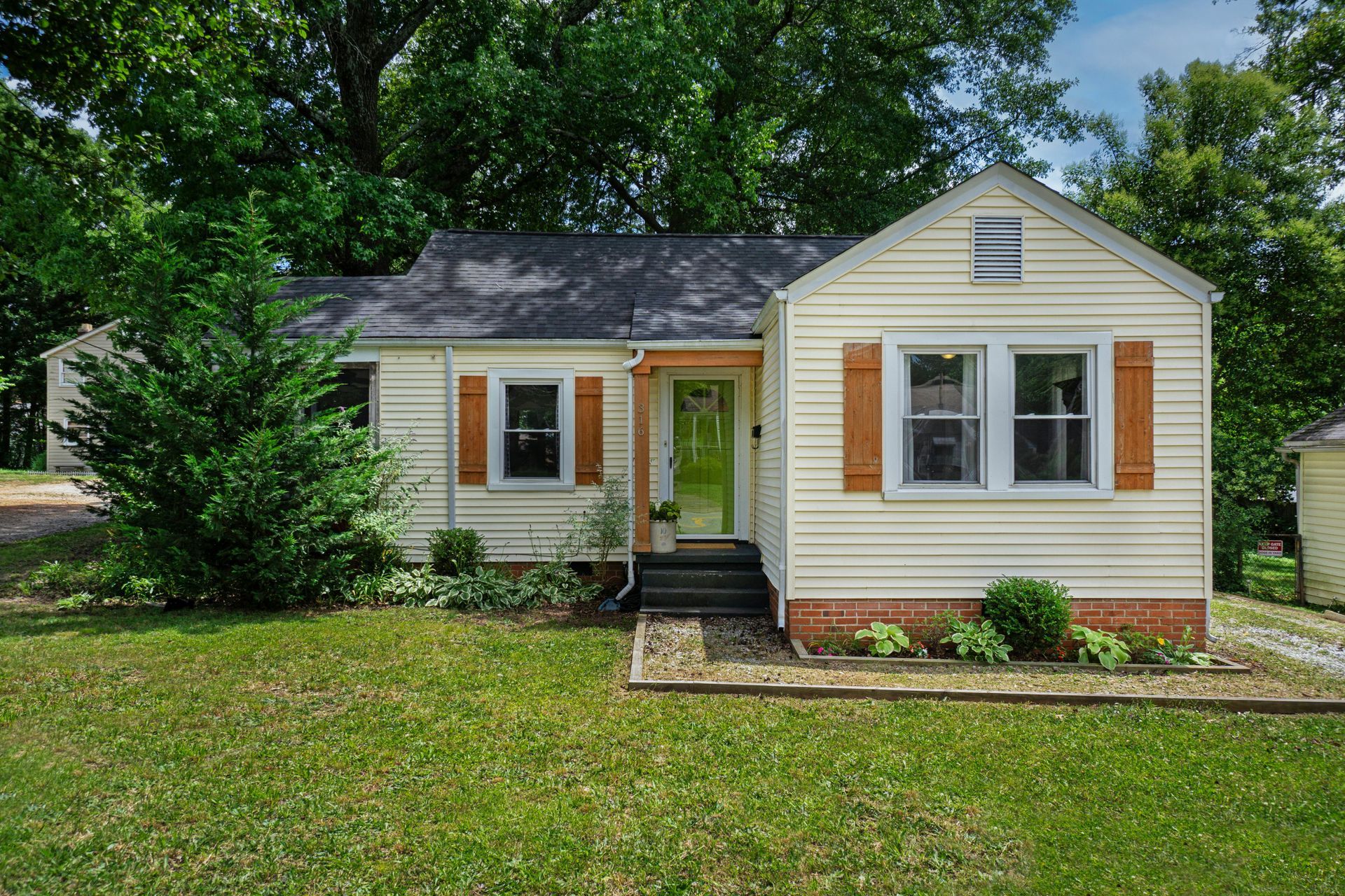 Small, yellow house with brown shutters, green door, and lush green yard.