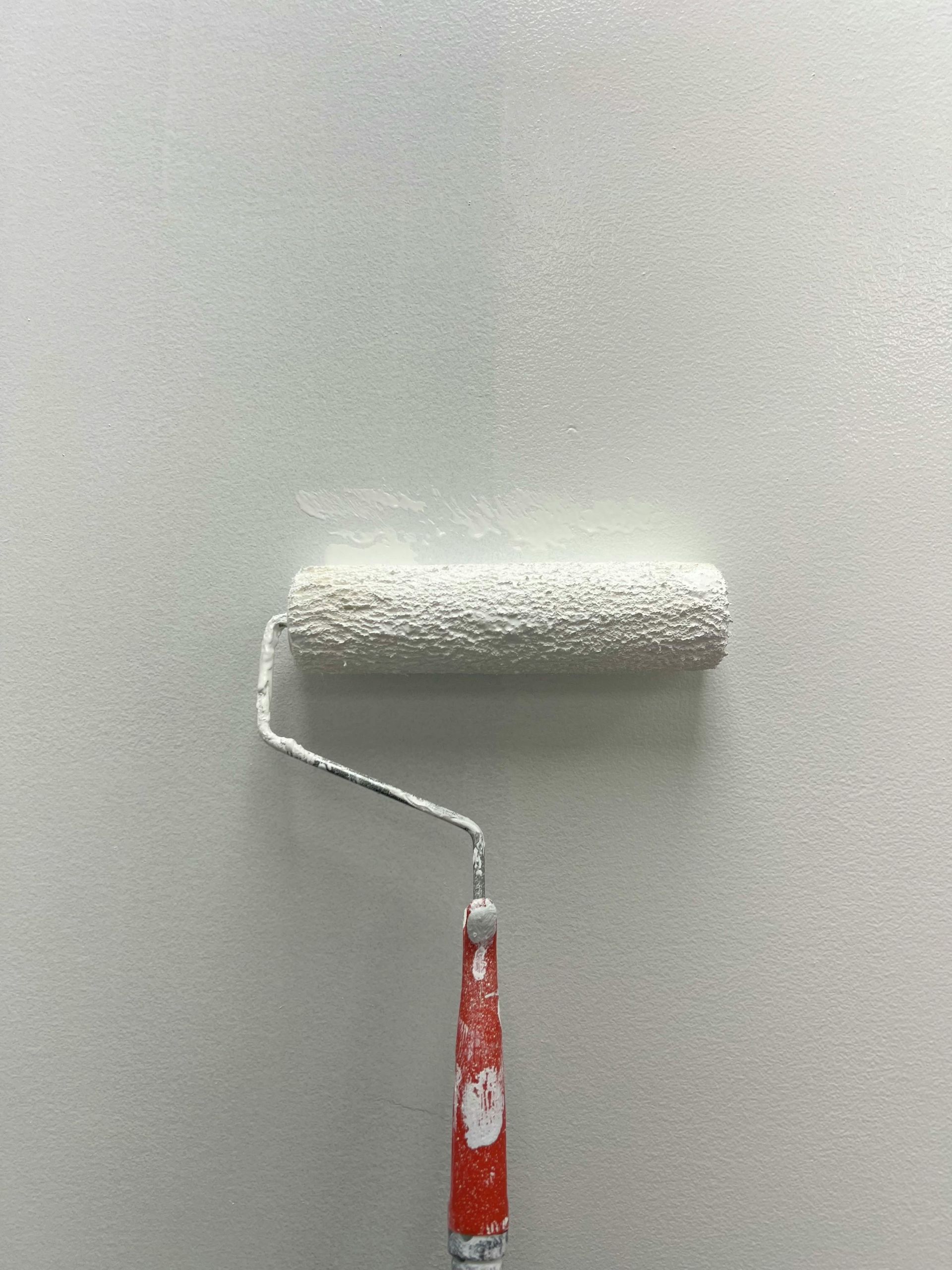 Paint roller applying white paint to a wall.