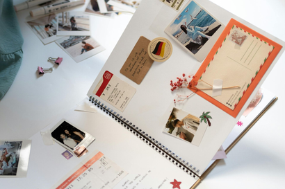 Een spiraalgebonden scrapbookpagina, versierd met foto's, stickers, een ansichtkaart en handgeschreven notities, ligt op een wit bureau.