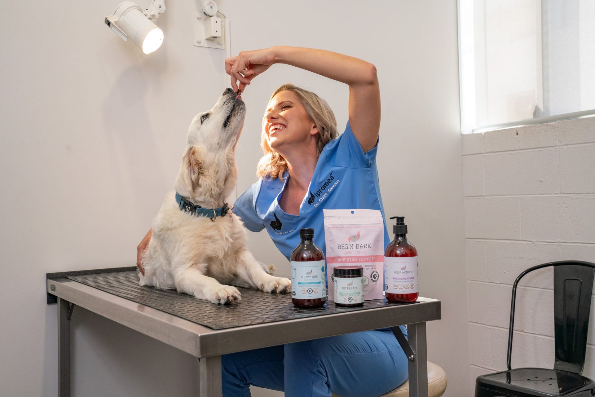 A woman is sitting at a table feeding a dog.