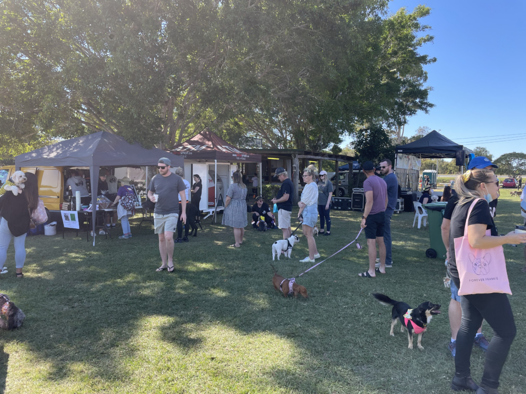 A group of people are standing in a park with their dogs.