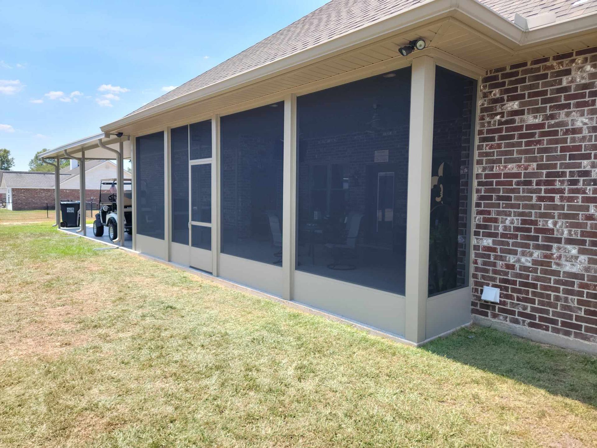 A screened in porch on the side of a brick house.