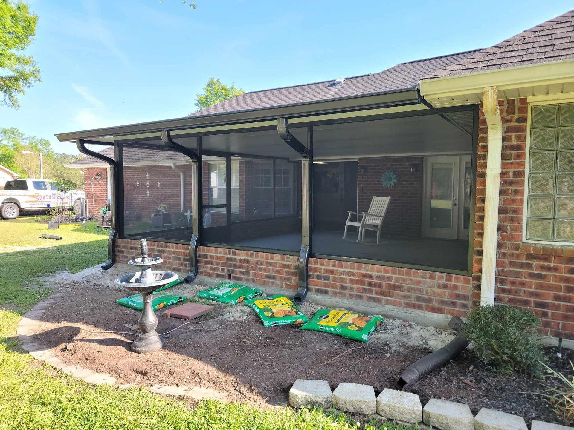 A brick house with a screened in porch and a bird bath.