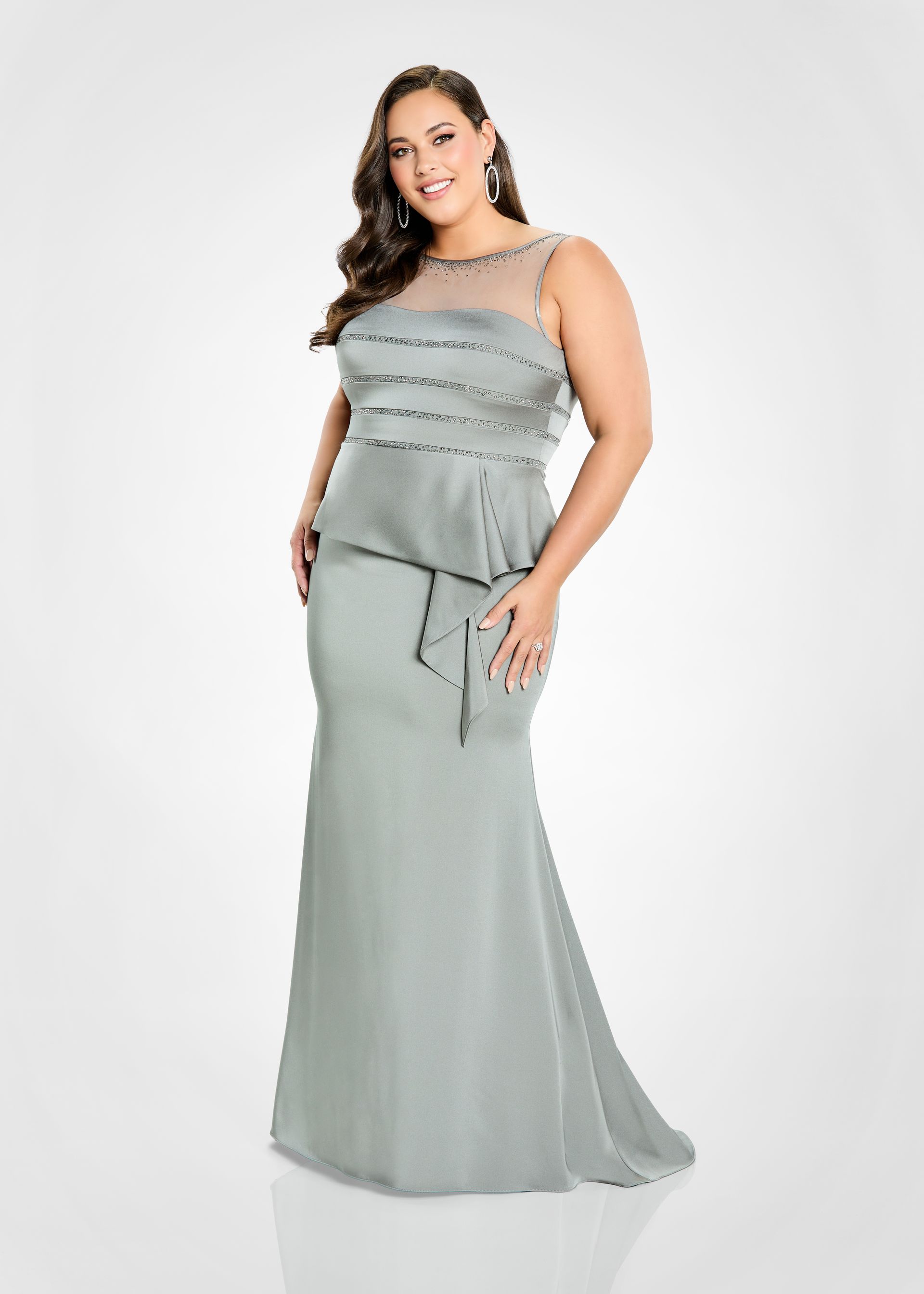 Woman in a navy blue formal gown, posed, looking at the viewer. Dress has a sheer neckline and a cascading ruffle.