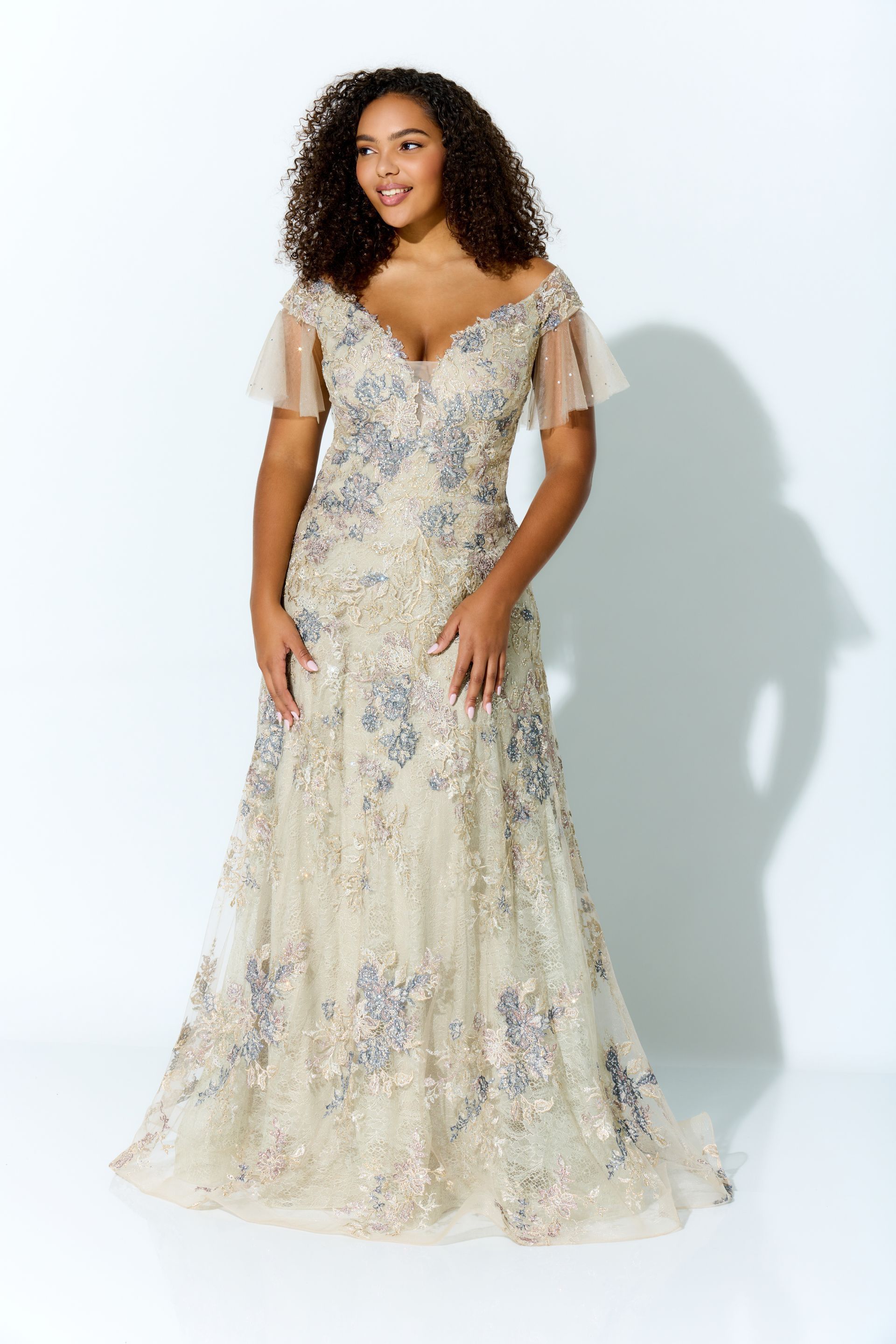 Woman wearing an off-the-shoulder, beaded formal gown, standing against a white backdrop.
