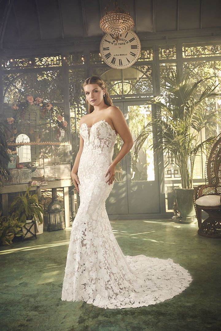 Woman in a strapless white lace wedding dress poses in an ornate greenhouse.