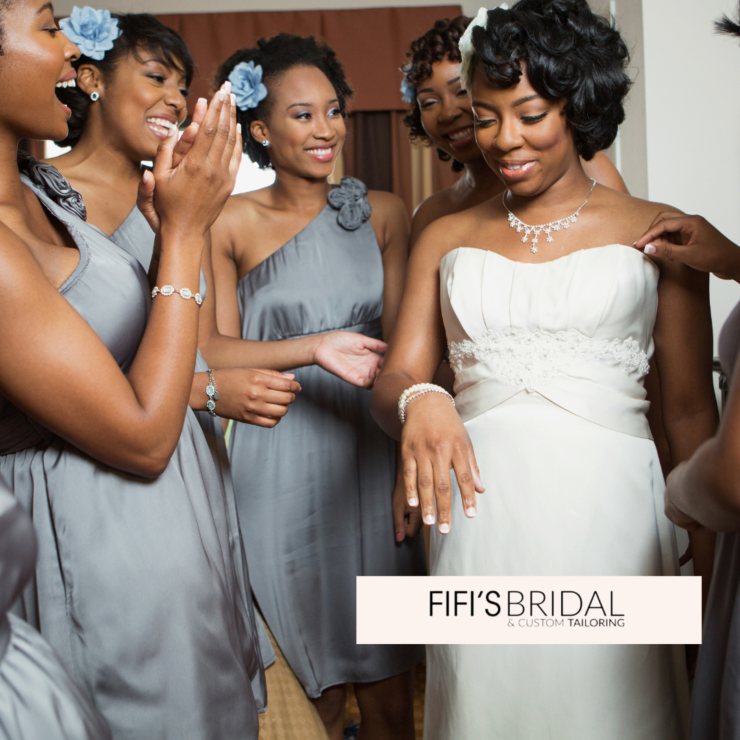 Bride surrounded by bridesmaids, wearing white gown and gray dresses.