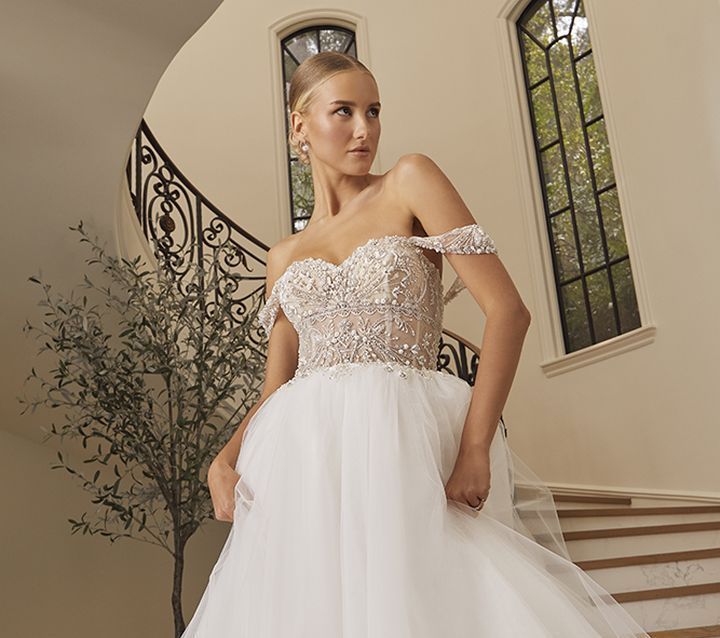 Woman in white off-the-shoulder wedding gown, standing on a curved staircase.
