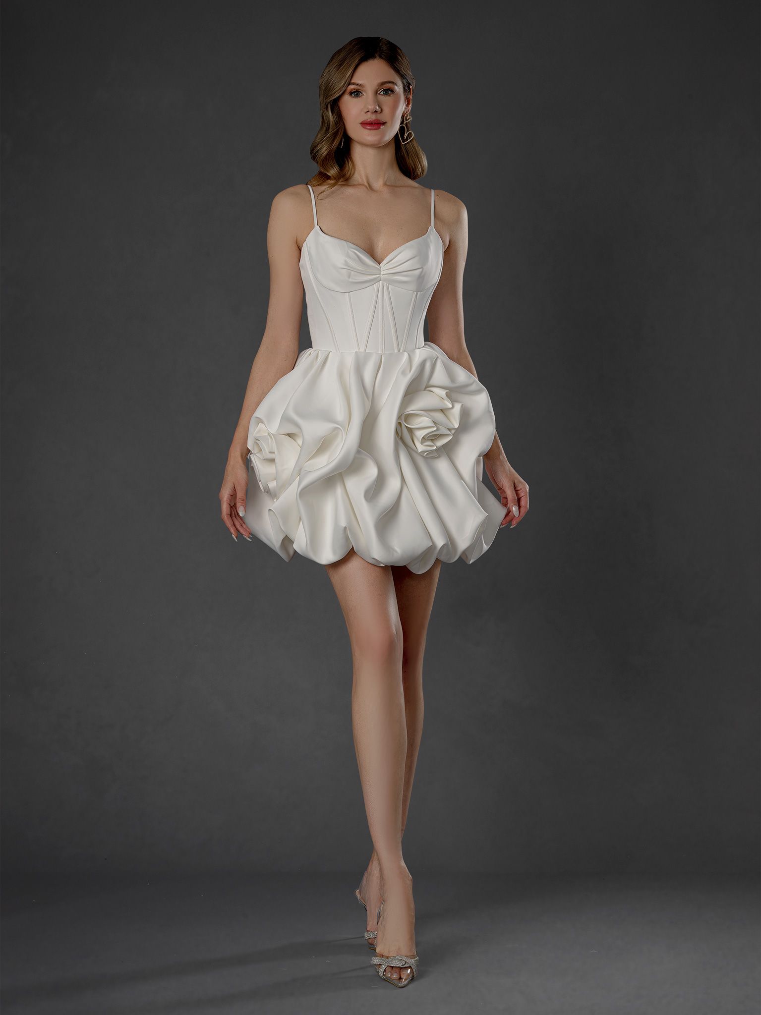 Woman in a white cocktail dress with spaghetti straps and a ruffled skirt, standing.