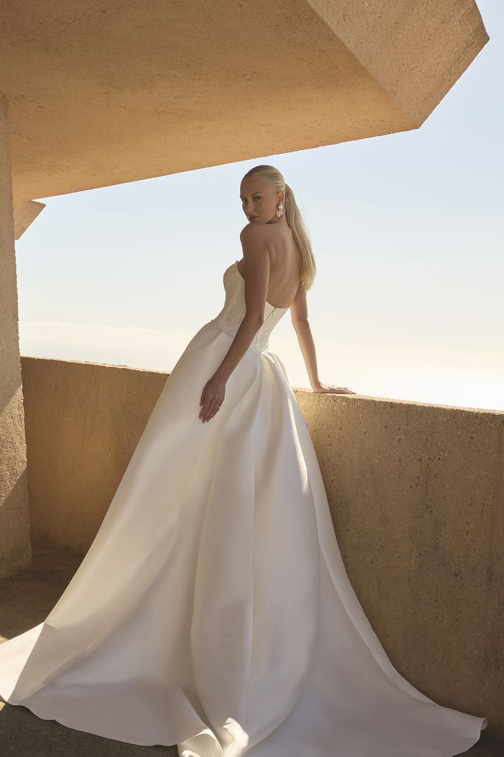 Woman in a strapless white wedding dress with detachable train, standing on a balcony.