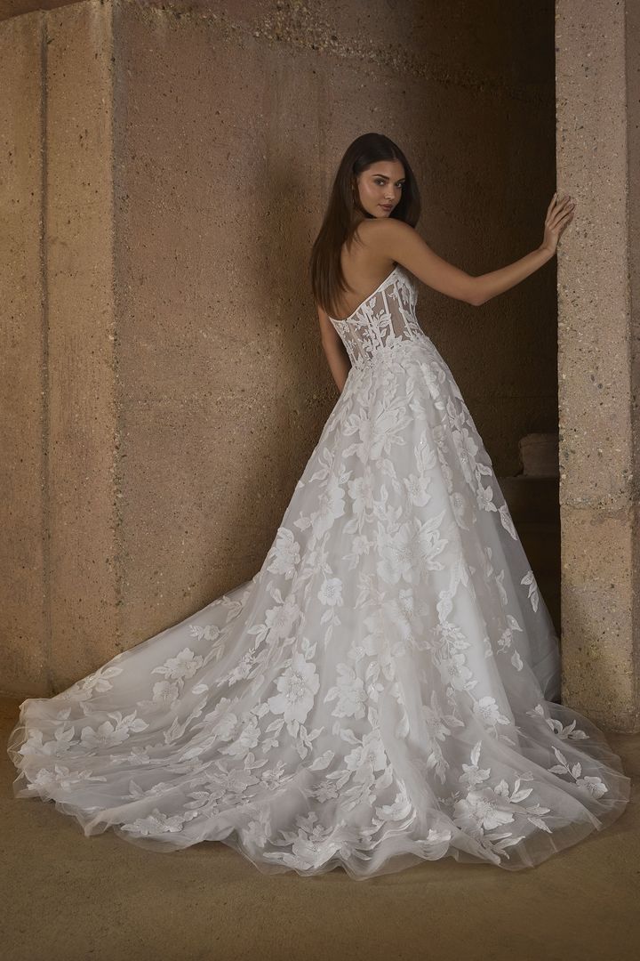 Woman in strapless white lace wedding dress, train on stone wall background.