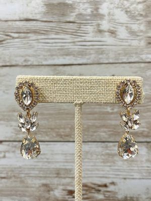 Gold-toned chandelier earrings with clear, faceted gemstones on a burlap jewelry stand against a wood background.