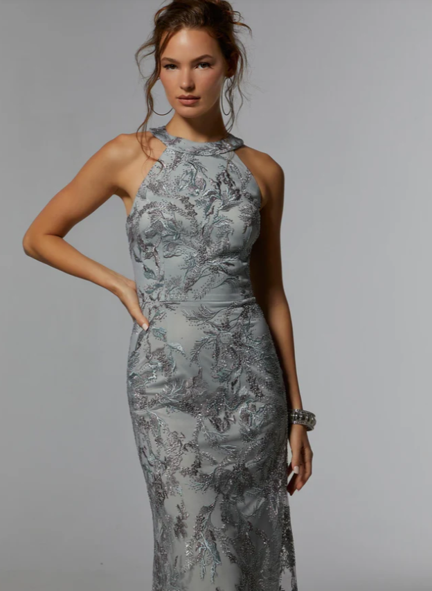 Woman in silver beaded gown, posing with hand on hip. Gray background.