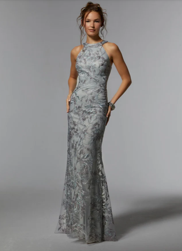 Woman in a silver, floral-patterned gown, posing in a studio. High neckline, fitted silhouette.