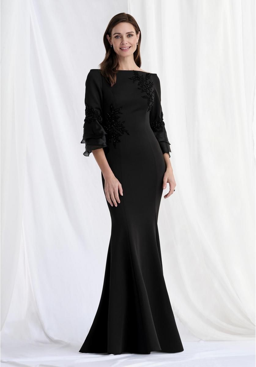 Woman in a black, floor-length gown with three-quarter sleeves, posed in front of a white backdrop.