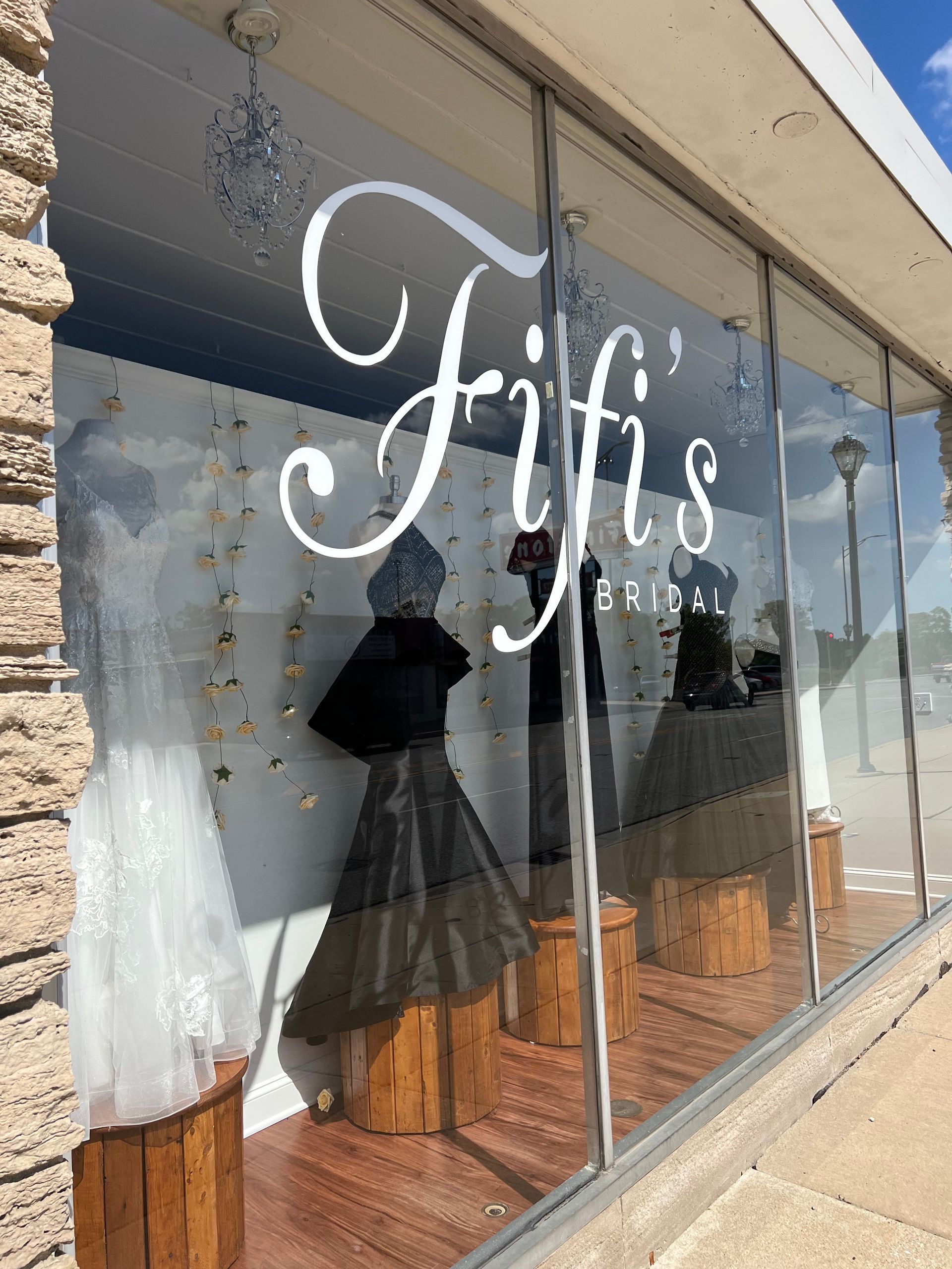 Fifi's bridal shop window display with dresses, featuring a white cursive logo.