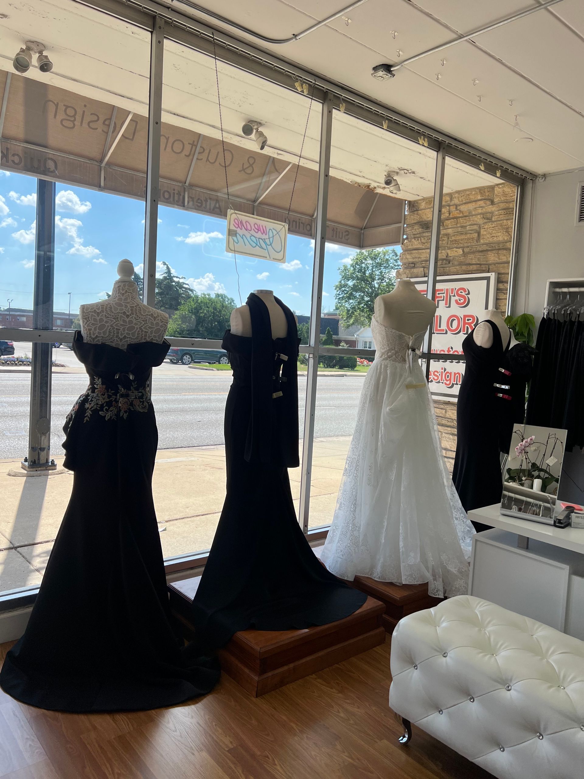 Formal dresses on display in a boutique window. Black and white gowns on mannequins; sunny outdoor view.