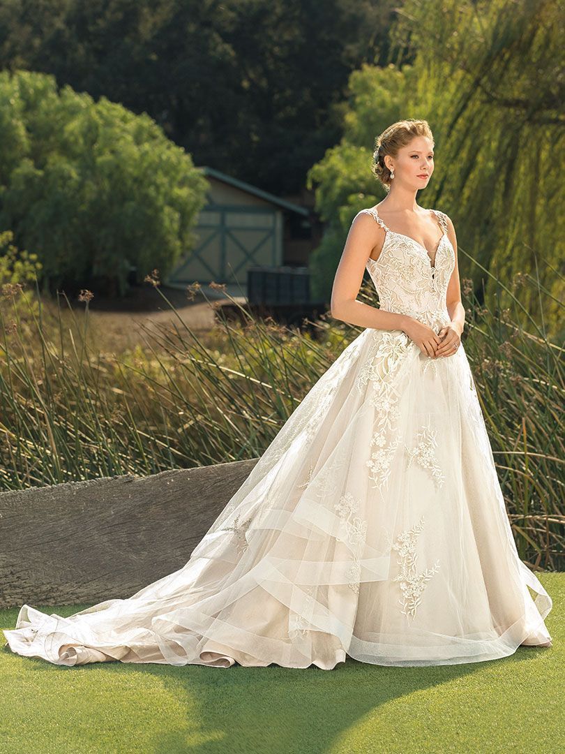 Woman in white wedding dress with train outdoors, standing in grass.