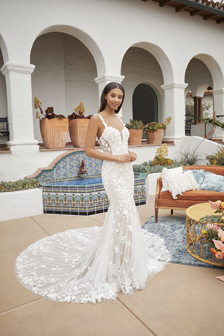 Woman in a white lace wedding dress poses outside by a fountain with arched architecture.