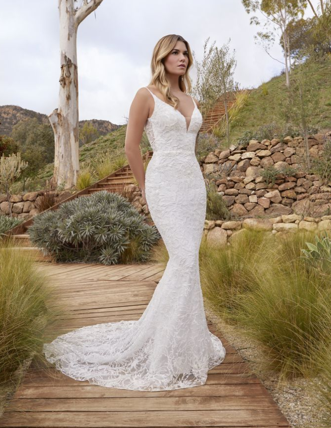 Woman in a white beaded wedding dress with a train, standing outdoors.
