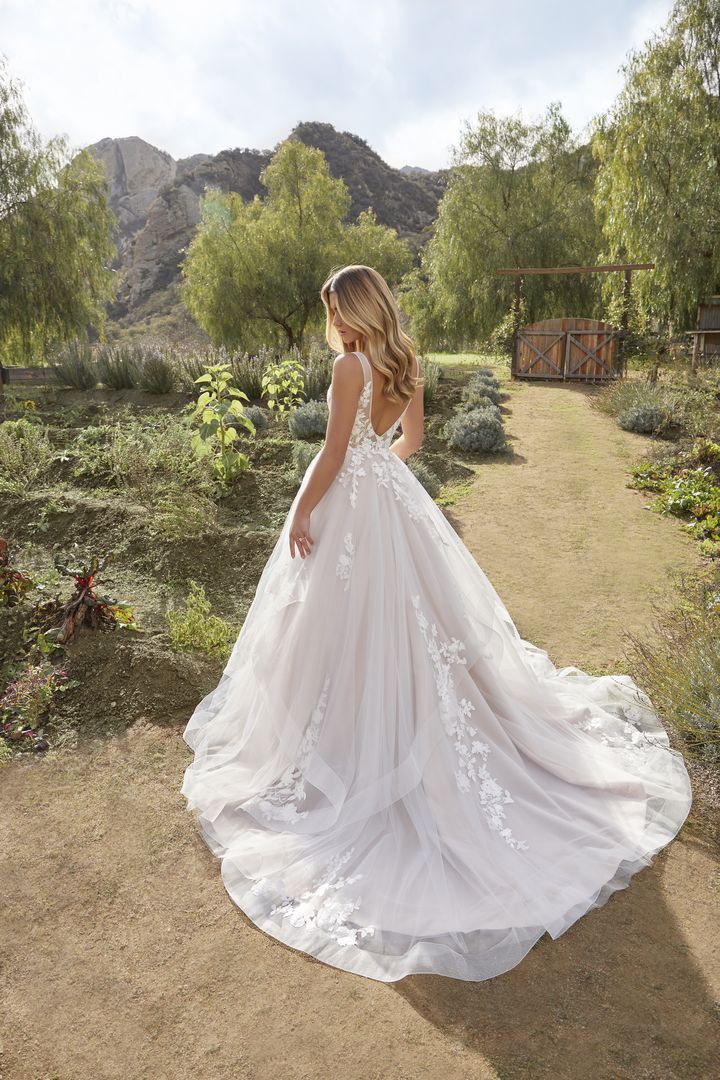 Woman in white wedding dress with floral bodice and flowing skirt, outdoors in a garden setting.