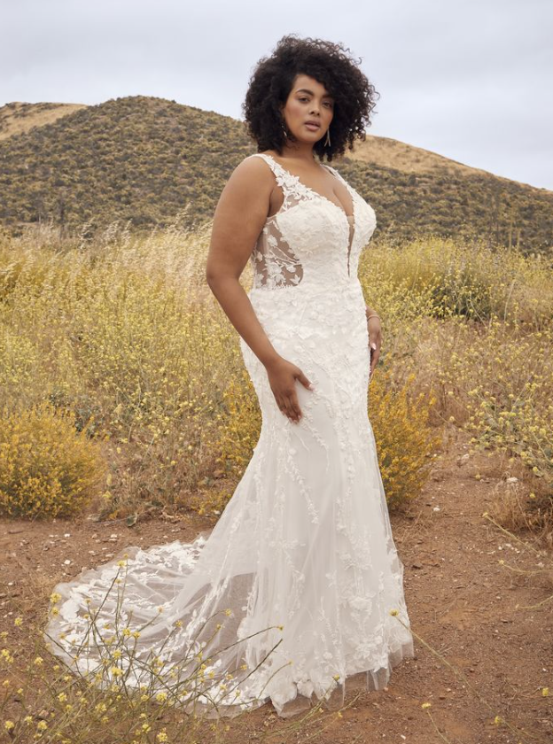 Woman in a white lace wedding dress poses outdoors.