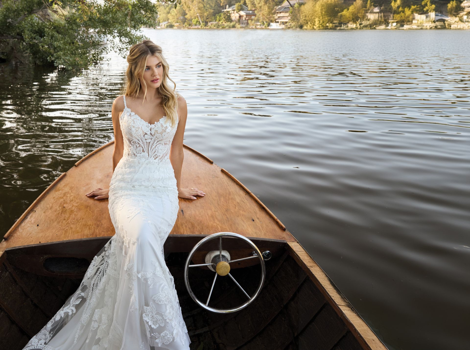 Woman in a white wedding dress sits in a wooden boat on a lake.