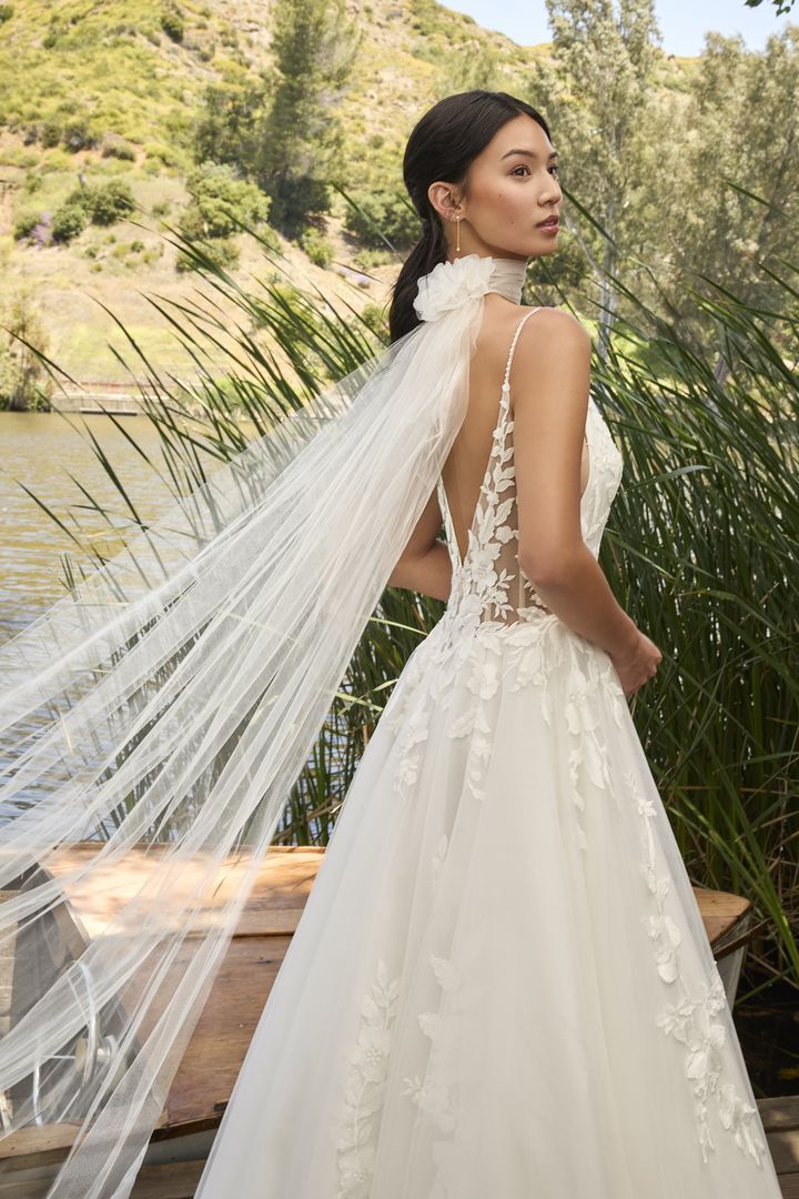 Woman in wedding dress with sheer veil, outdoors near water.