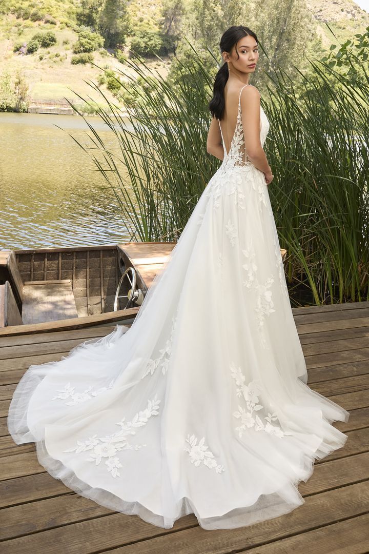 Woman in wedding dress with sheer veil, outdoors near water.
