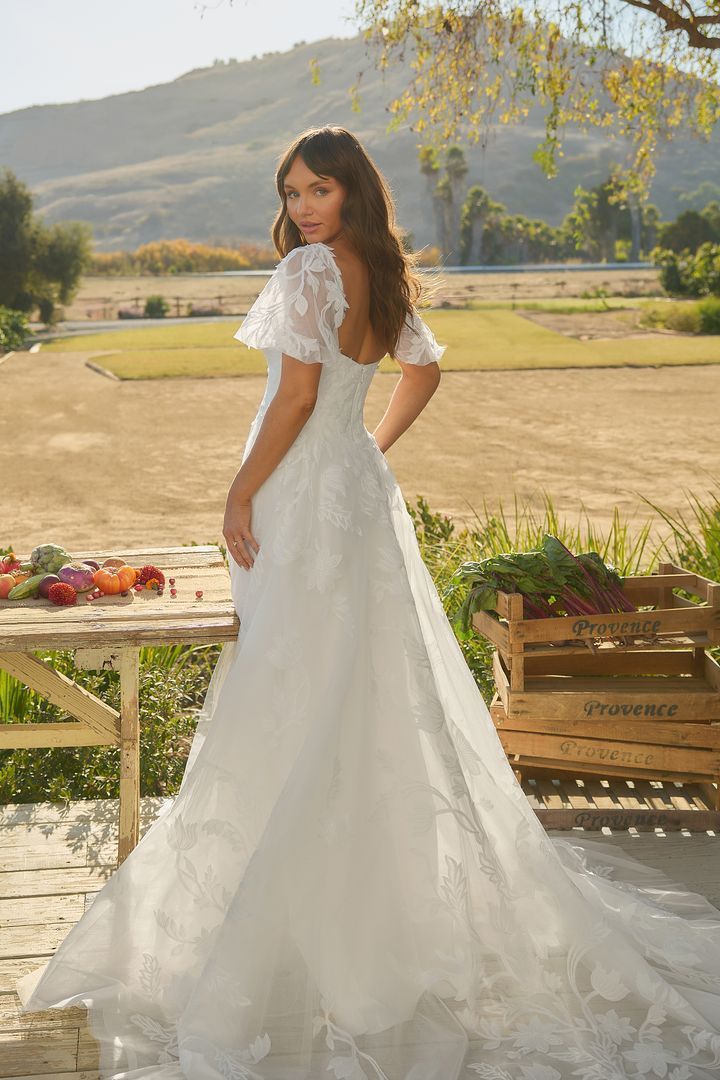 Woman in a white wedding dress with a train, standing outdoors.