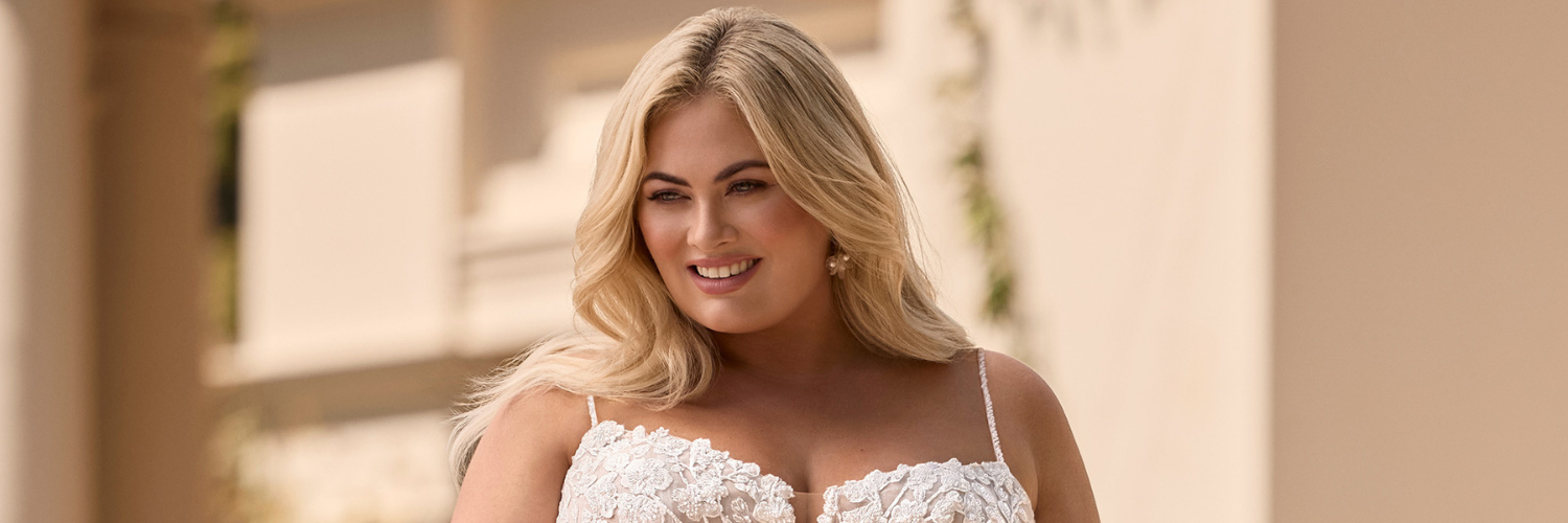Blonde woman wearing a white wedding dress smiles, outdoors.