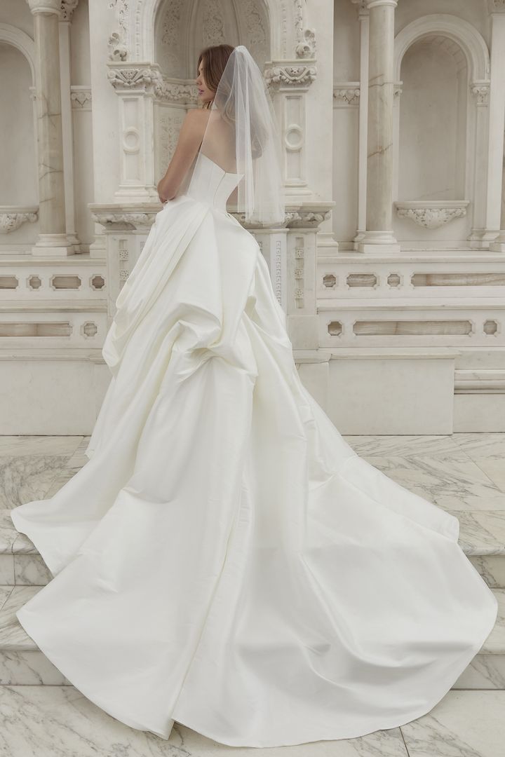 Bride in white satin wedding gown, standing on marble steps, short veil.