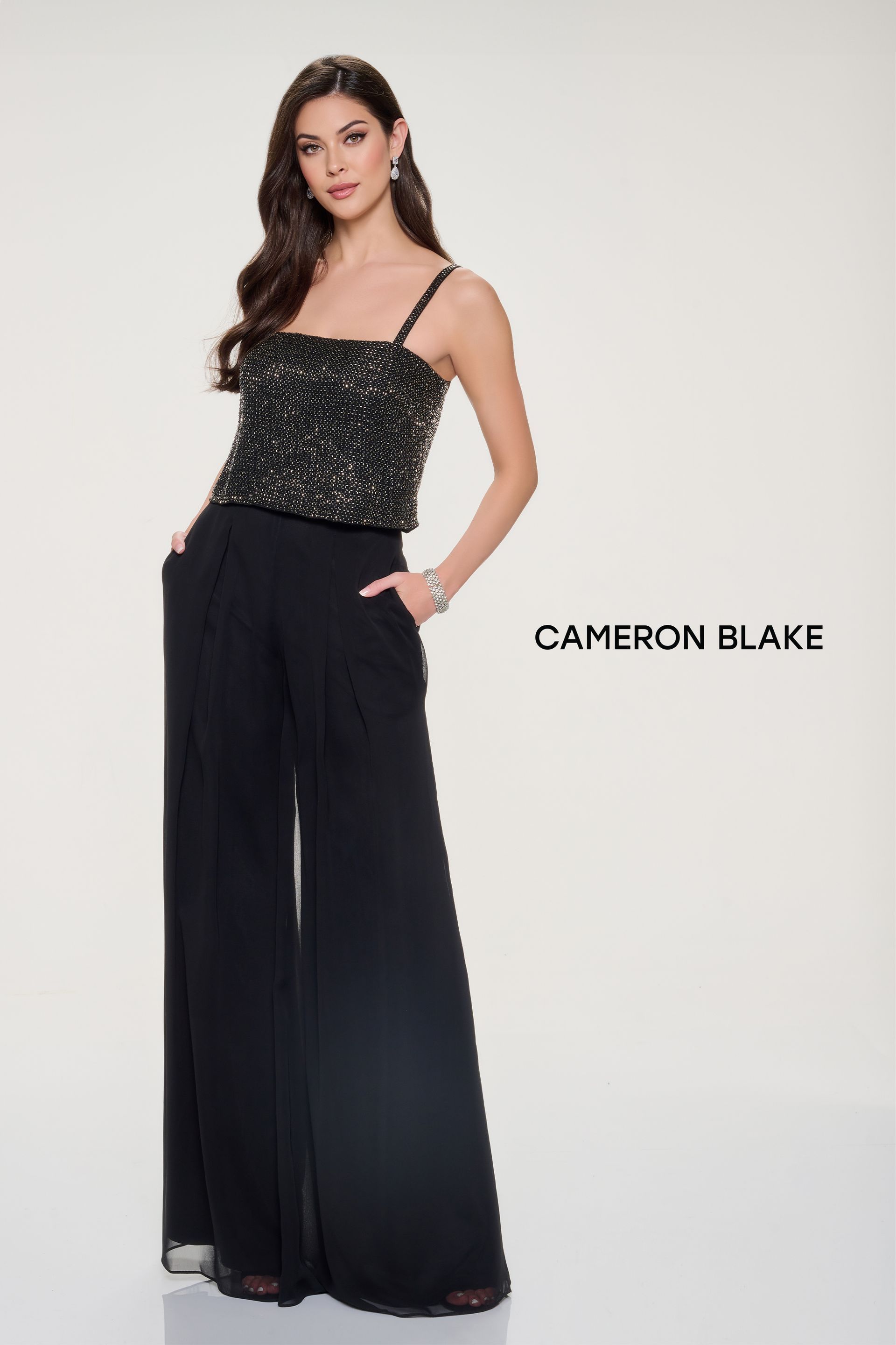 Woman in a black and gold sequin top with wide-leg black pants, standing, posing for a formal occasion.